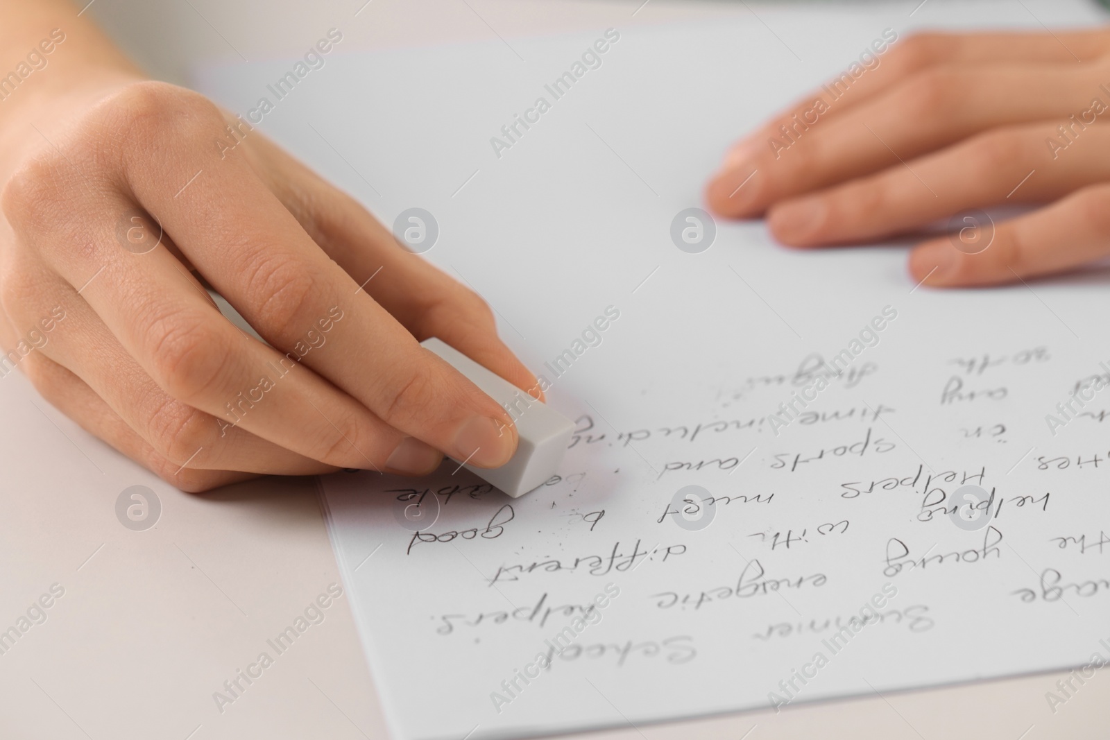 Photo of Girl erasing mistake in her notebook at white desk, closeup