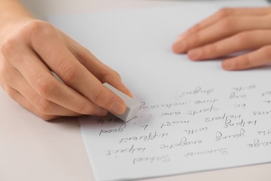 Girl erasing mistake in her notebook at white desk, closeup