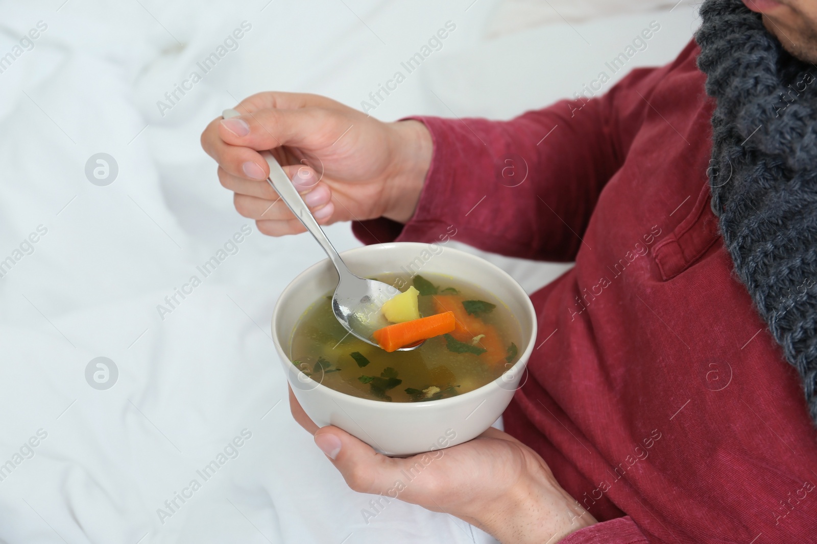 Photo of Sick young man eating broth to cure cold in bed at home