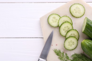 Photo of Cucumbers, dill, knife and marble cutting board on white wooden table, top view. Space for text