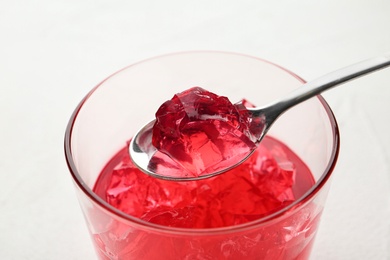 Spoon with fruit jelly over glass on light background, closeup