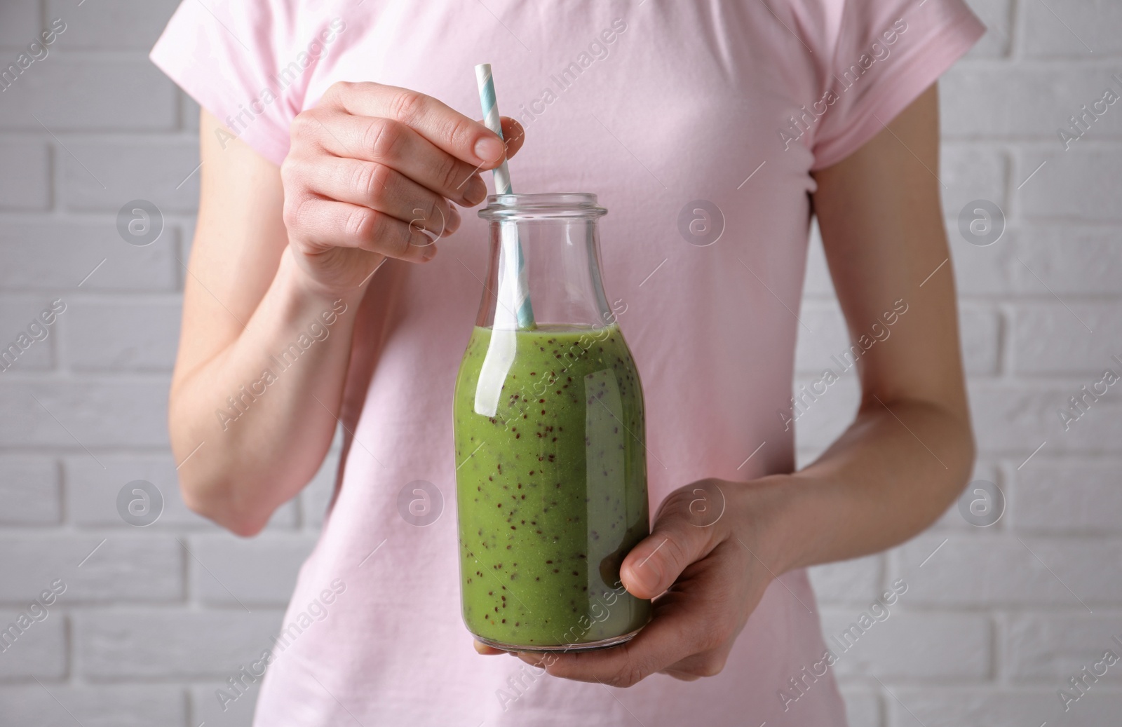 Photo of Woman with delicious kiwi smoothie near white brick wall, closeup