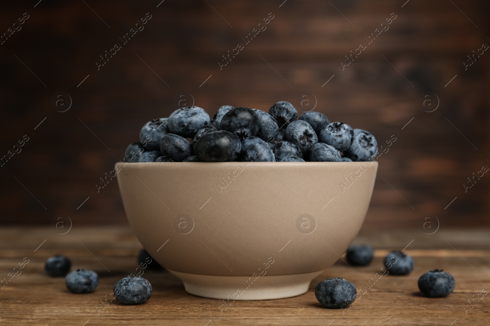 Photo of Ceramic bowl with blueberries on wooden table. Cooking utensil