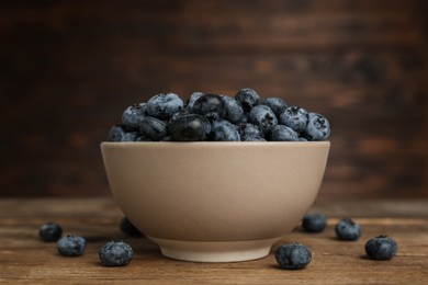 Photo of Ceramic bowl with blueberries on wooden table. Cooking utensil