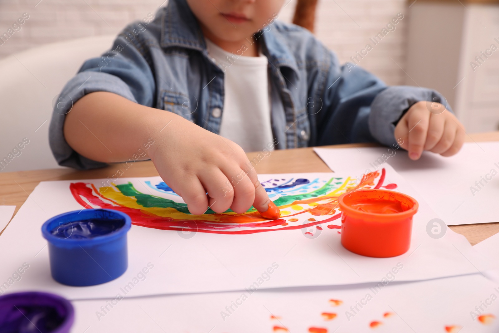 Photo of Little child painting with finger at wooden table indoors, closeup