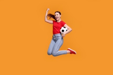 Photo of Emotional soccer fan with ball jumping on orange background