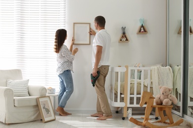 Photo of Happy couple decorating baby room with pictures together. Interior design