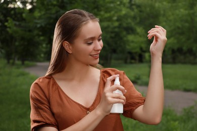 Photo of Woman applying insect repellent onto arm in park. Tick bites prevention