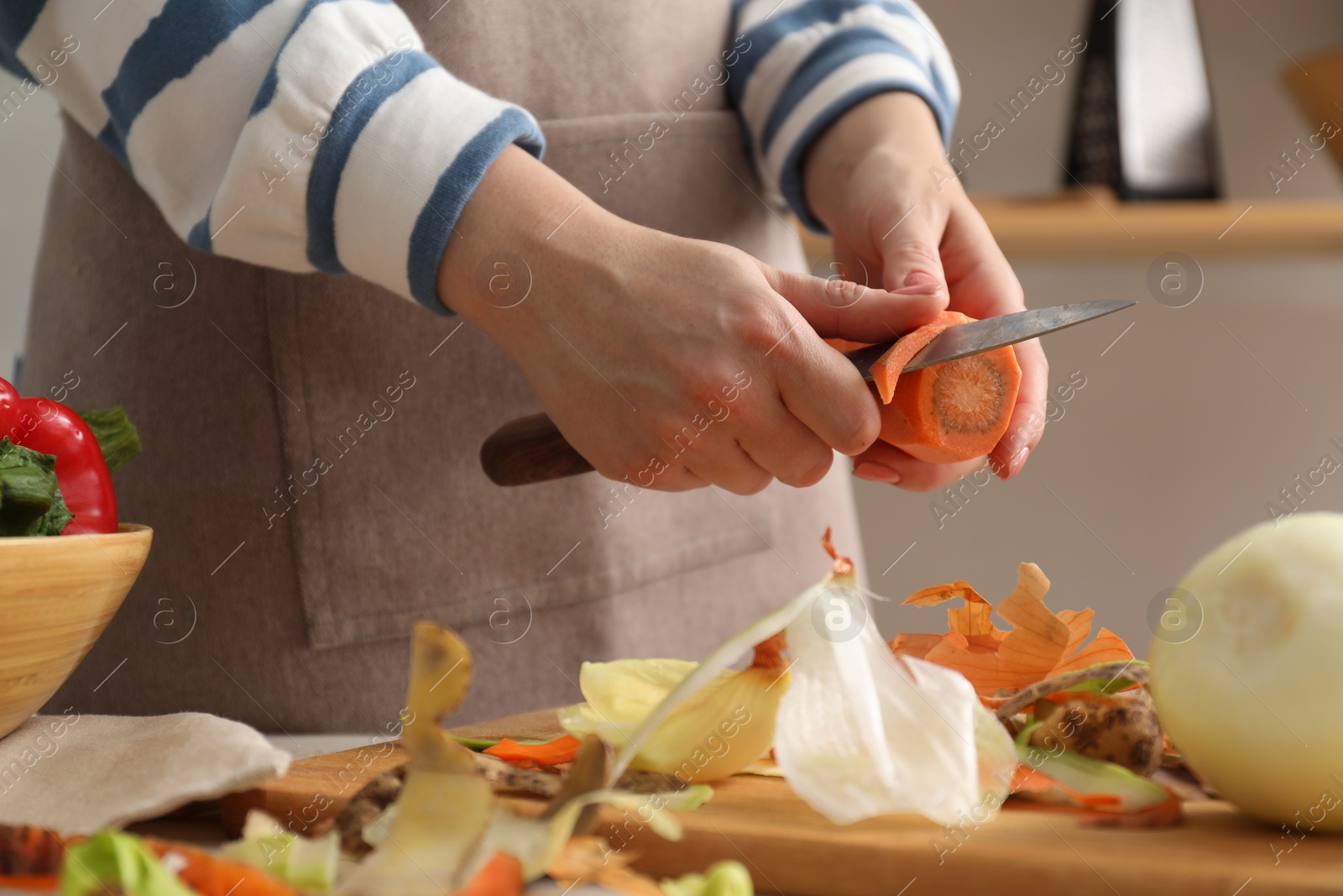 Photo of Woman peeling fresh carrot with knife at table in kitchen, closeup