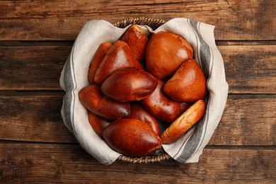 Delicious baked pirozhki in wicker basket on wooden table, top view