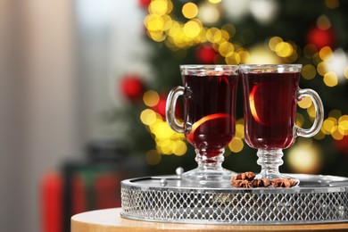 Photo of Hot mulled wine in glass cups and anise stars on table against blurred lights. Space for text