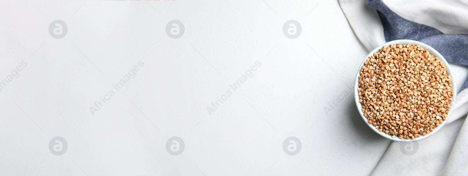 Image of Uncooked green buckwheat grains in bowl on white table, top view with space for text. Banner design