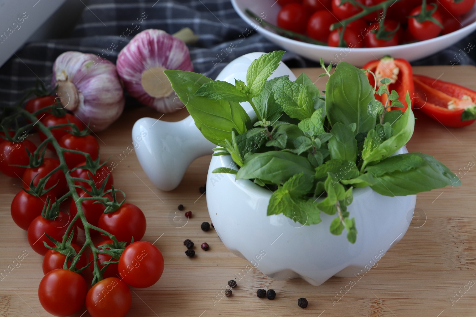 Photo of Mortar with different fresh herbs near pepper, garlic and cherry tomatoes on wooden table, closeup