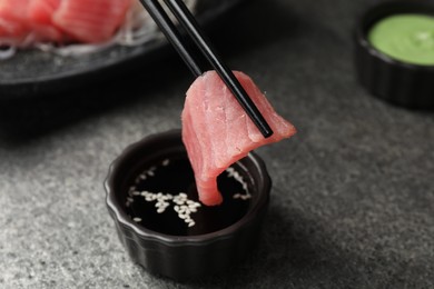 Photo of Dipping tasty sashimi (piece of fresh raw tuna) into soy sauce at gray table, closeup