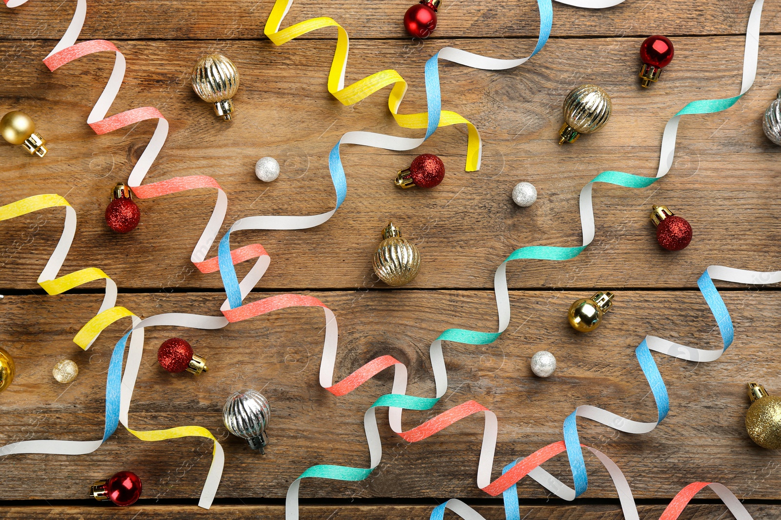 Photo of Colorful serpentine streamers and Christmas balls on wooden background, flat lay