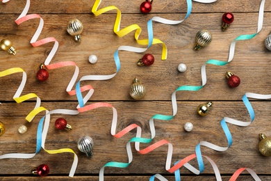 Colorful serpentine streamers and Christmas balls on wooden background, flat lay