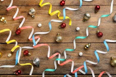 Photo of Colorful serpentine streamers and Christmas balls on wooden background, flat lay