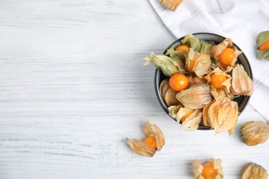 Photo of Ripe physalis fruits with dry husk on white wooden table, flat lay. Space for text