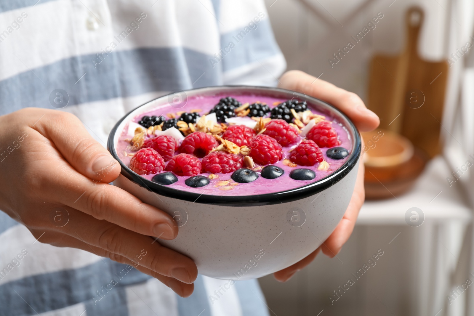 Photo of Woman holding bowl with tasty acai smoothie and berries on blurred background, closeup