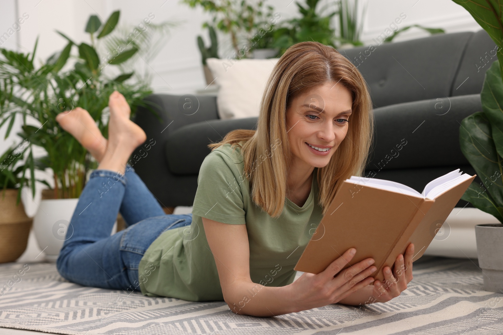 Photo of Woman reading book on floor in room with beautiful houseplants