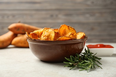 Delicious sweet potato chips in bowl and rosemary on table