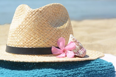 Photo of Stylish straw hat with flower, seashell on towel, closeup. Beach accessories