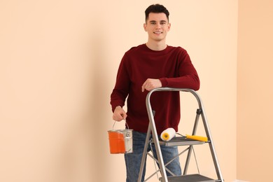 Young handsome man with paint can near metal stepladder indoors, space for text. Room renovation