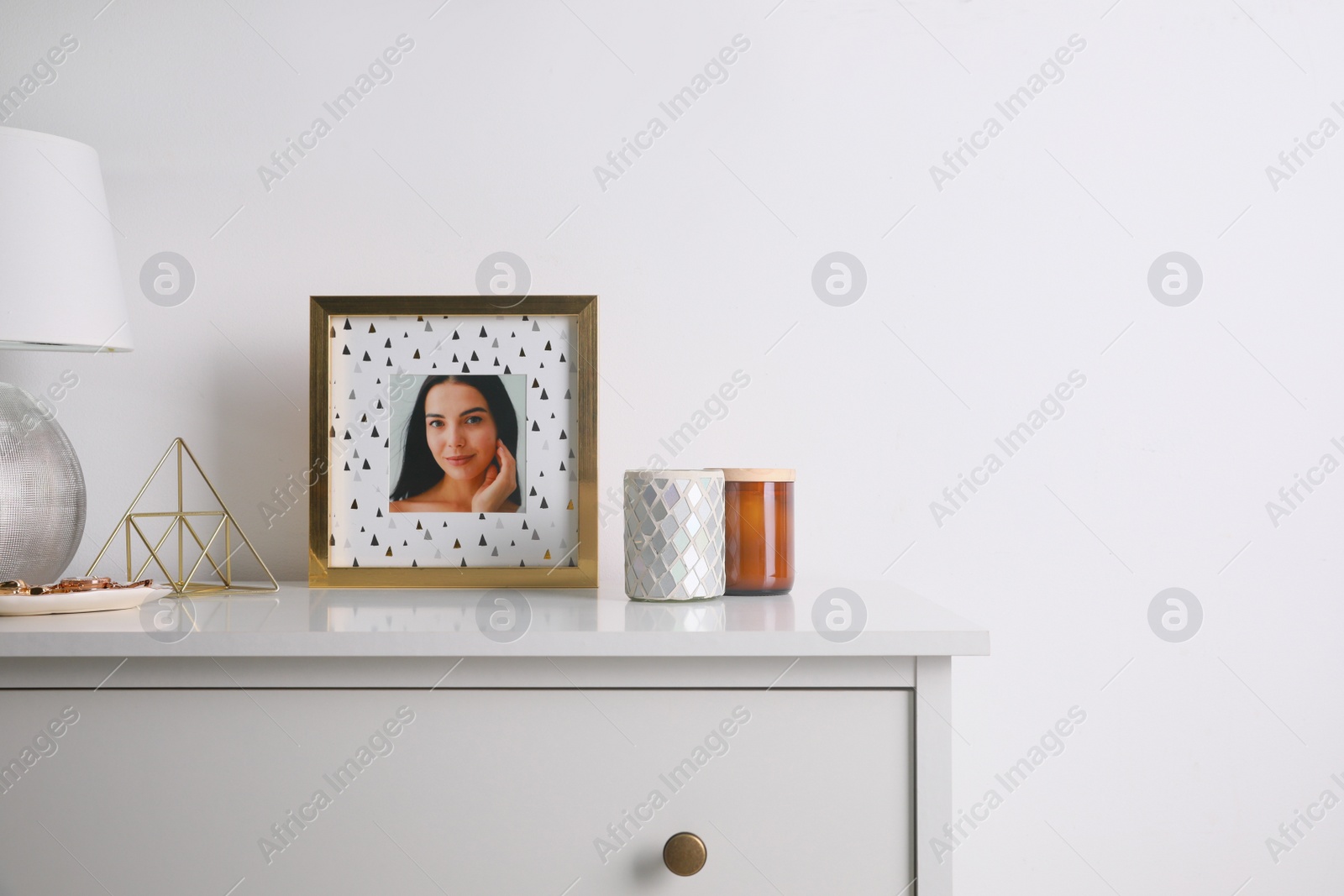 Photo of Photo frame with portrait of beautiful young woman near stylish decor on white commode. Space for text