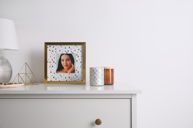 Photo of Photo frame with portrait of beautiful young woman near stylish decor on white commode. Space for text