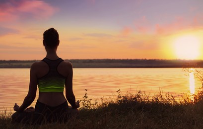 Image of Woman meditating near river at sunset, back view. Practicing yoga
