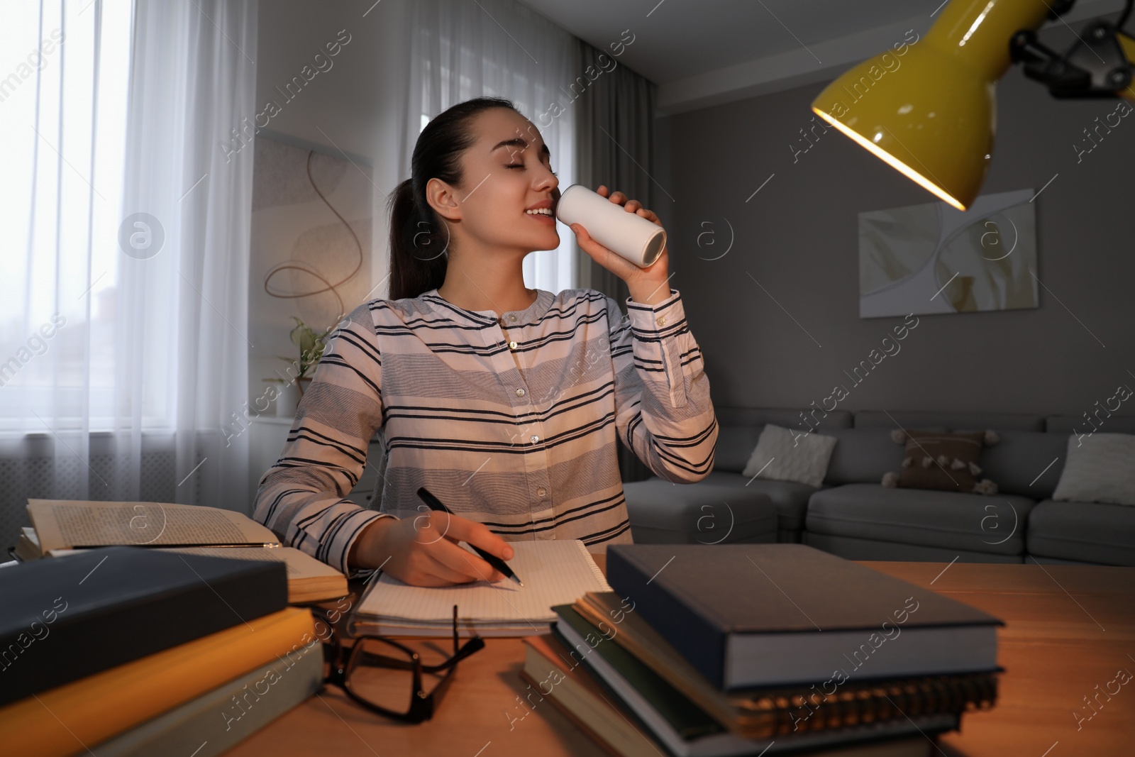 Photo of Young woman with energy drink studying at home