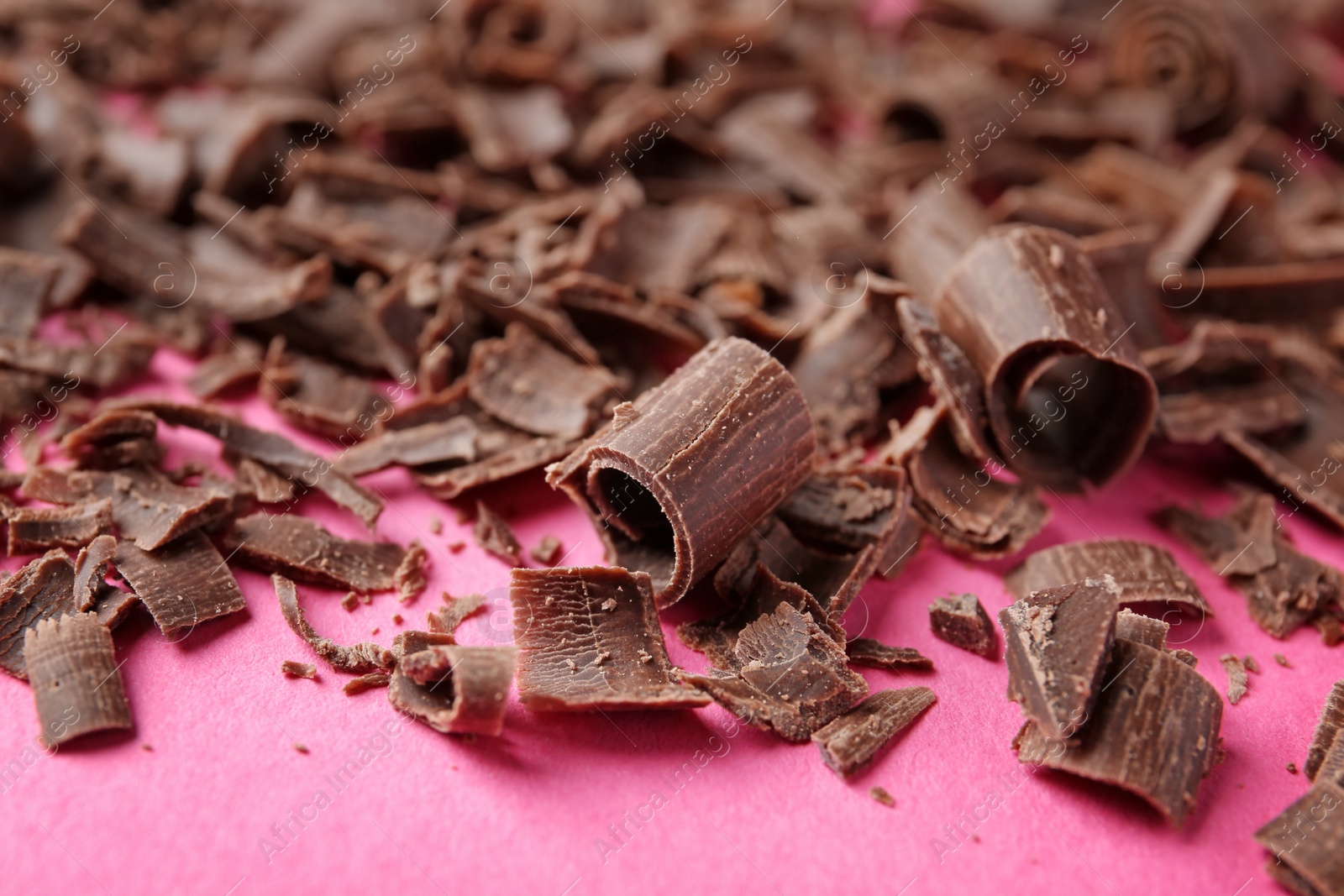 Photo of Curls of tasty chocolate on color background, closeup