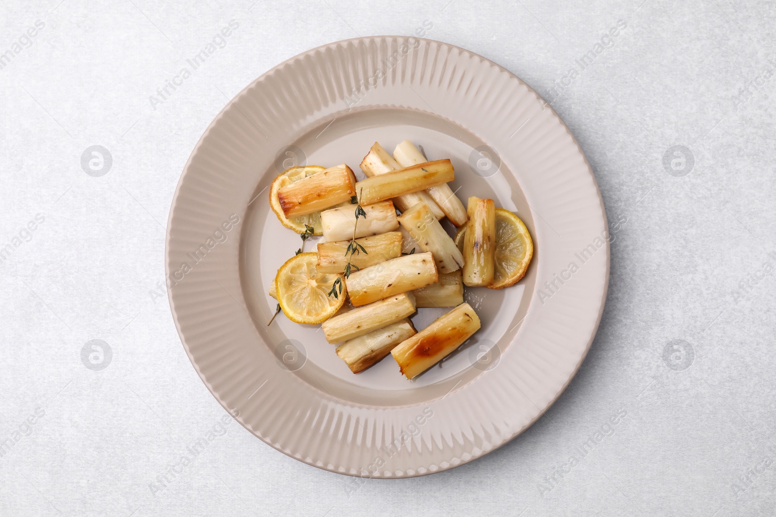 Photo of Plate with baked salsify roots, lemon and thyme on light grey table, top view