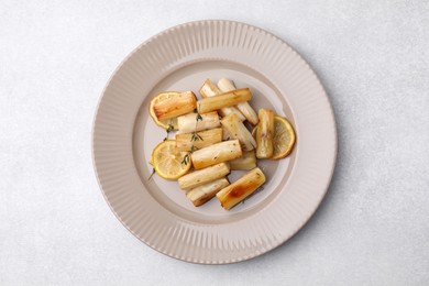 Plate with baked salsify roots, lemon and thyme on light grey table, top view