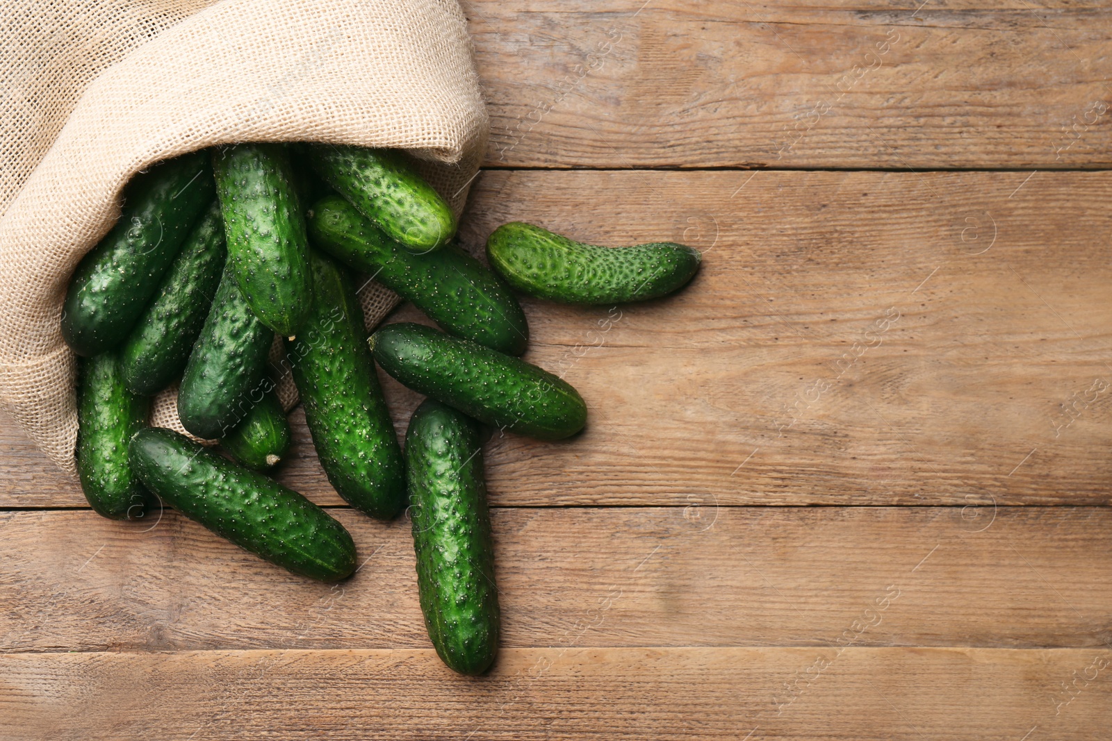 Photo of Fresh ripe cucumbers in sack on wooden table, flat lay. Space for text