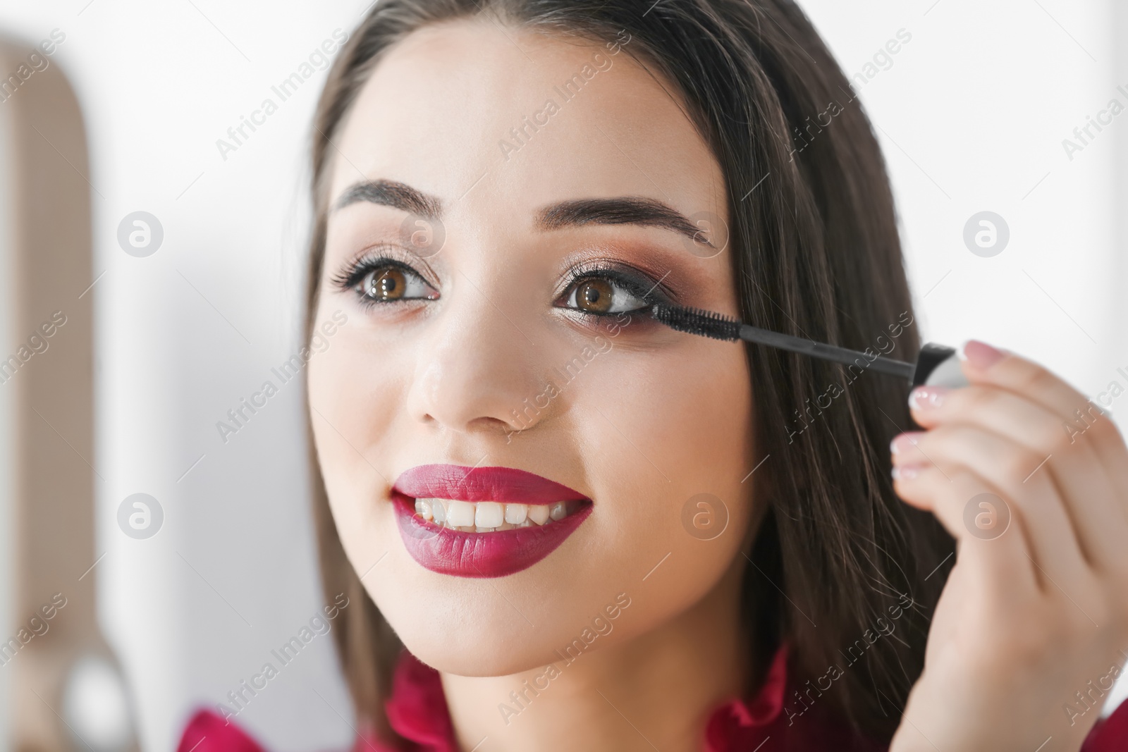 Photo of Portrait of beautiful woman applying makeup on blurred background