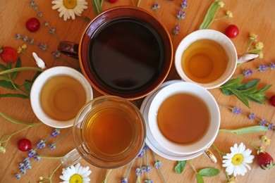 Photo of Cups with tasty herbal tea, different flowers and fruits on wooden table, flat lay