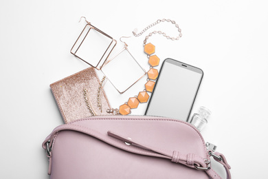 Stylish woman's bag with smartphone and accessories on white background, flat lay