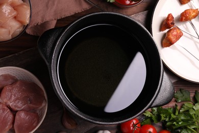 Photo of Fondue pot, forks with fried meat pieces and other products on wooden table, flat lay