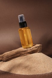 Photo of Bottle of serum and tree bark on sand against brown background