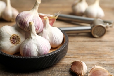 Photo of Fresh organic garlic in bowl on wooden table, closeup