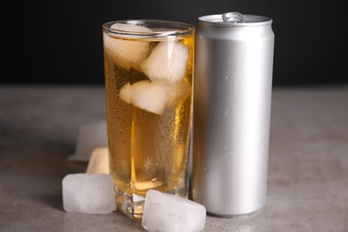 Photo of Tasty energy drink with ice cubes in glass and aluminium can on grey table, closeup