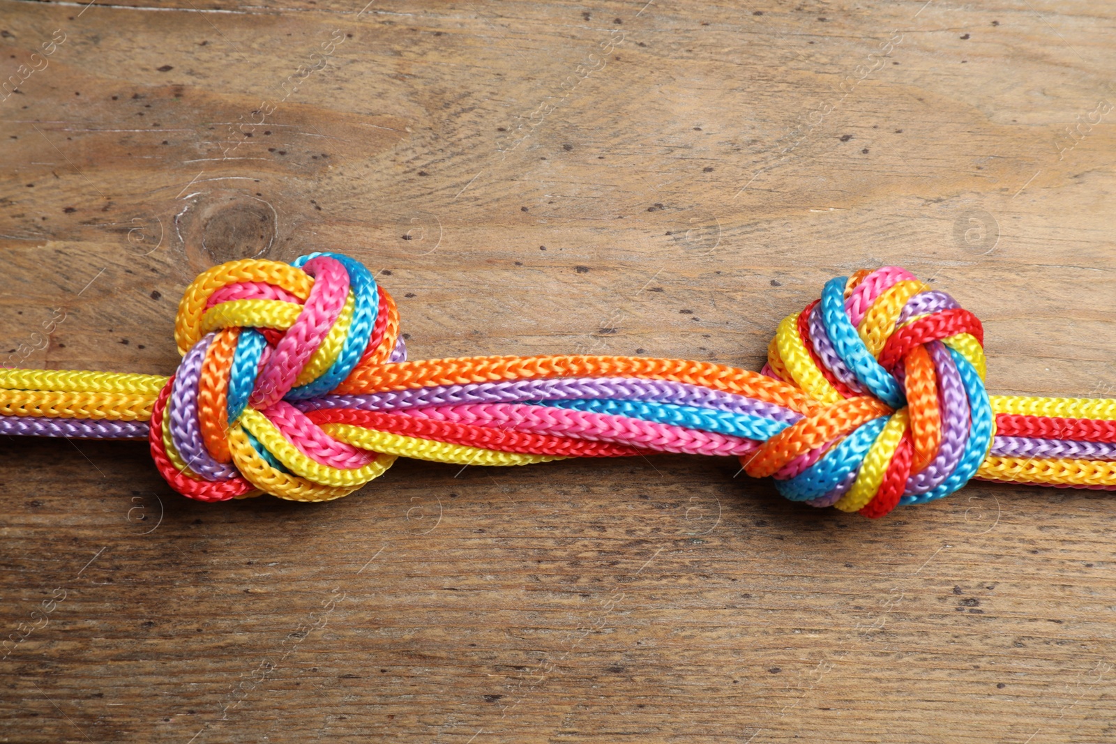 Photo of Colorful ropes tied together on wooden background, top view. Unity concept