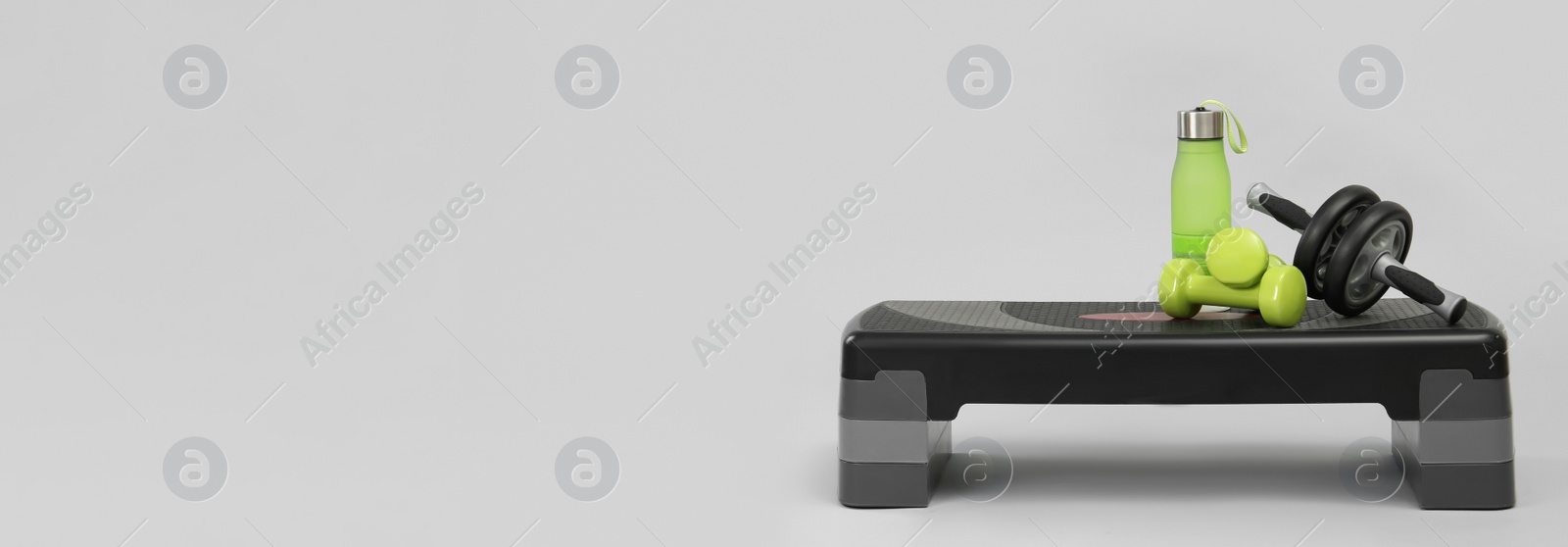 Image of Step platform, water bottle, dumbbells and abdominal wheel on light background, space for text. Banner design