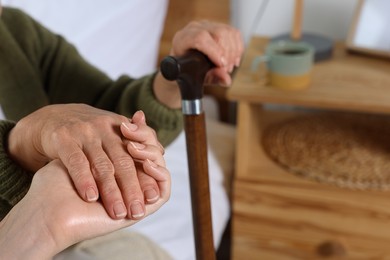 Photo of Caregiver and elderly woman with walking cane at home, closeup
