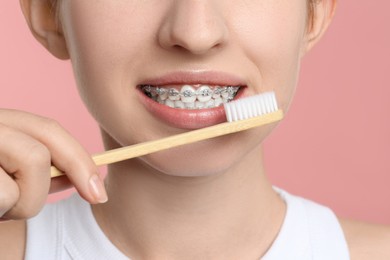 Woman with dental braces cleaning teeth on pink background, closeup