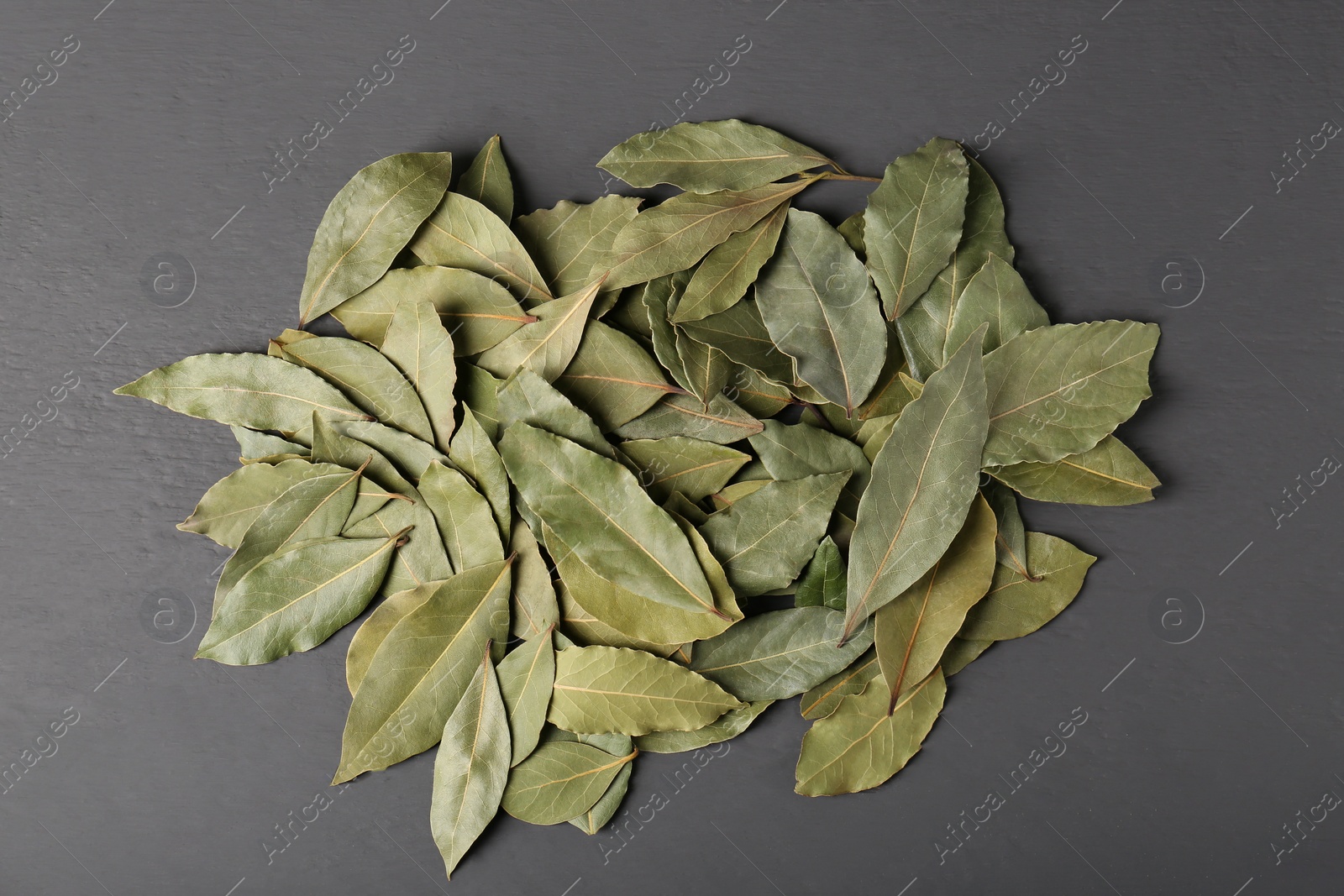 Photo of Pile of aromatic bay leaves on gray wooden table, top view