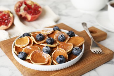 Photo of Delicious mini pancakes cereal with blueberries served on white marble table