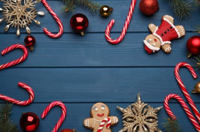 Frame of tasty candy canes and Christmas decor on blue wooden table, flat lay. Space for text