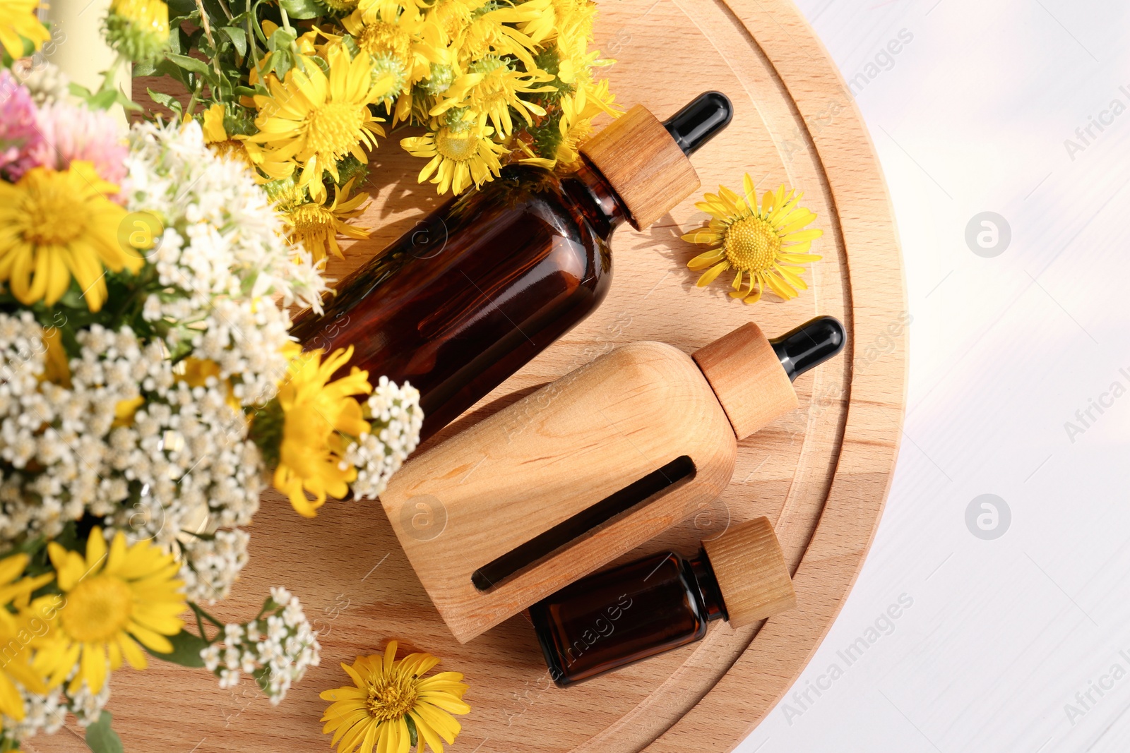 Photo of Glass bottles of essential oil and different wildflowers on white wooden table, top view